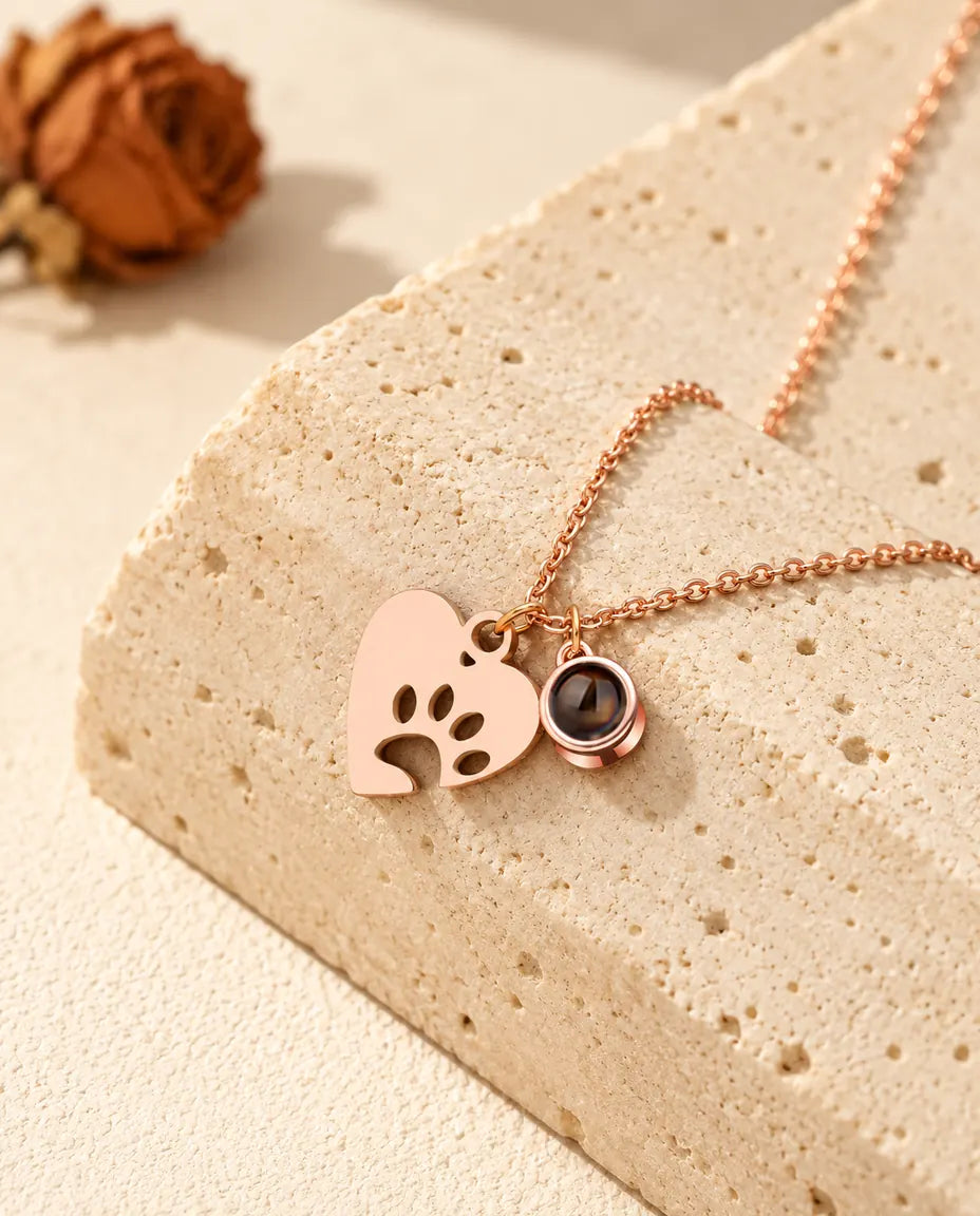Rose gold tone paw print heart and projection stone charm resting against a travertine block