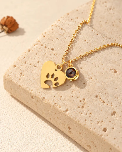 Gold tone paw print heart necklace with a projection stone charm on travertine