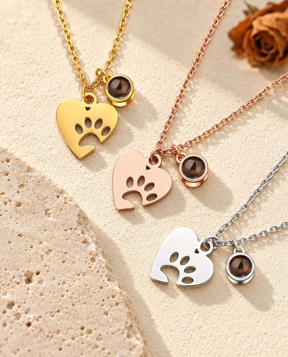 Gold tone, rose gold tone and silver tone paw print heart necklaces beside a travertine slab