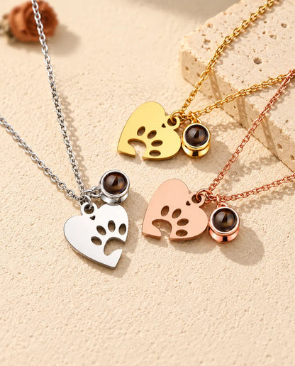Silver tone, gold tone and rose gold tone paw heart necklaces arranged by a travertine slab