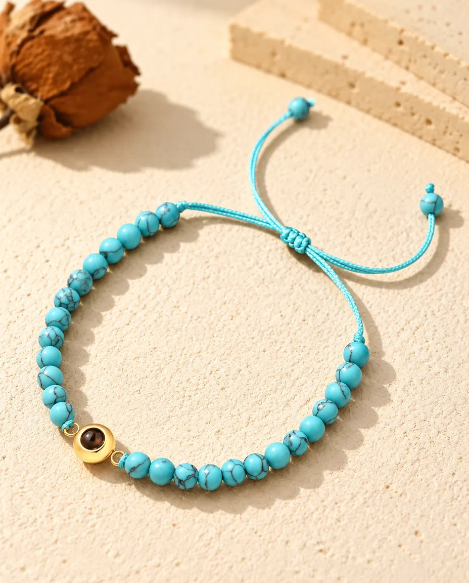 Personalized photo projection bead bracelet with blue marbled beads and a gold tone ring charm on cream plaster