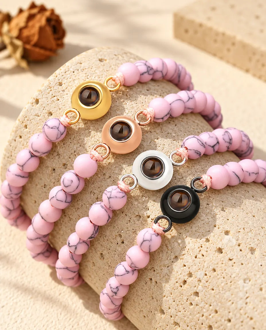 Pink marbled bead projection bracelets with four charm colors draped over travertine