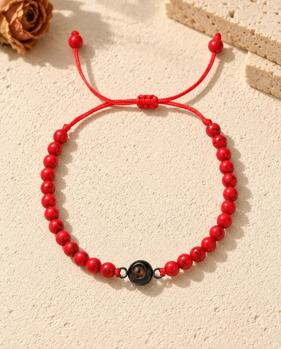 Top view of the red bead projection bracelet with a black ring charm and sliding knot