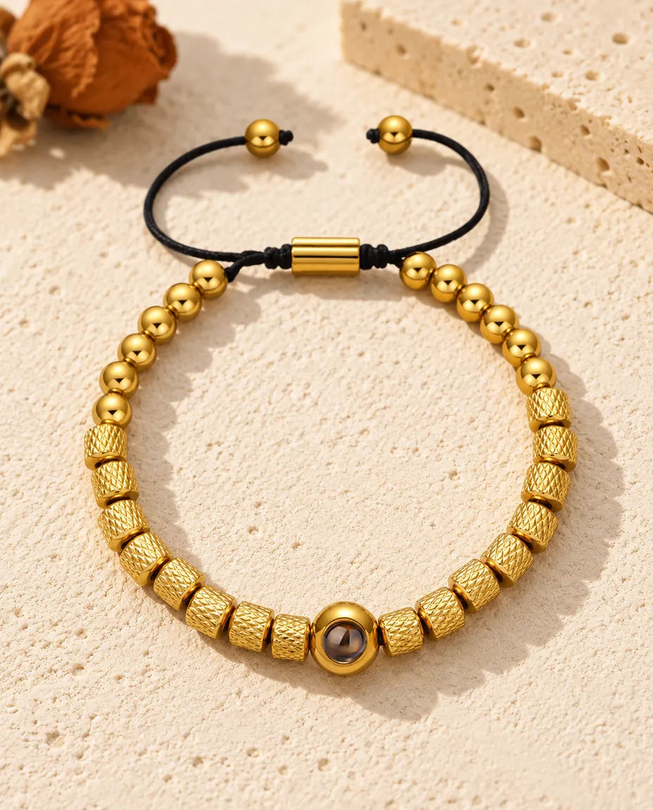 Personalized photo projection bead bracelet in gold tone with textured barrel beads and a sliding cord, on cream plaster