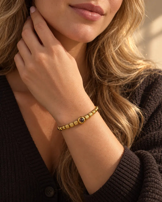 Woman touching the side of her neck, wearing the gold tone textured bead projection bracelet