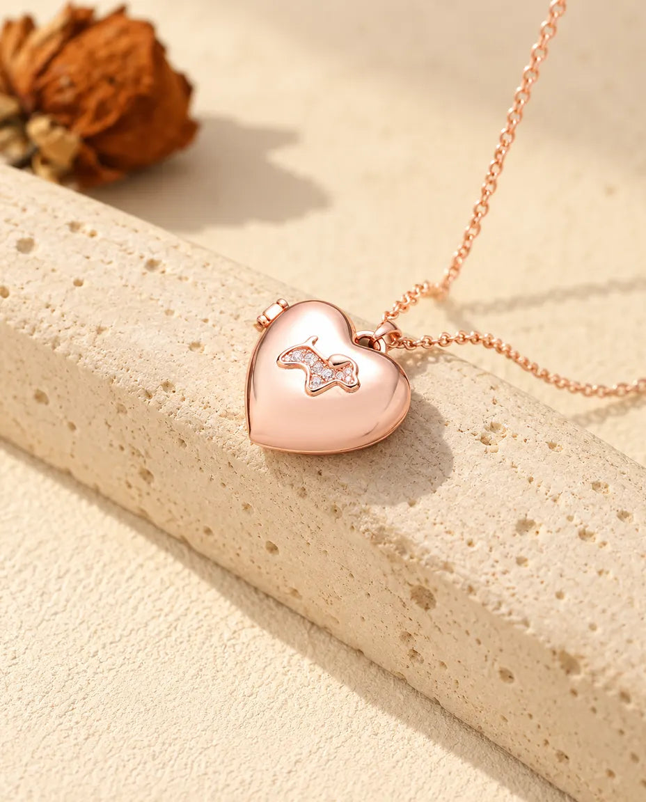 Rose gold tone puppy heart photo locket necklace on travertine in warm sunlight