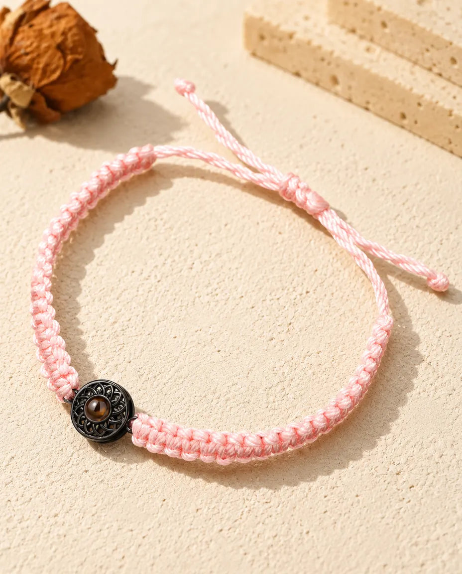Pink braided cord bracelet with a black round charm holding a brown projection stone