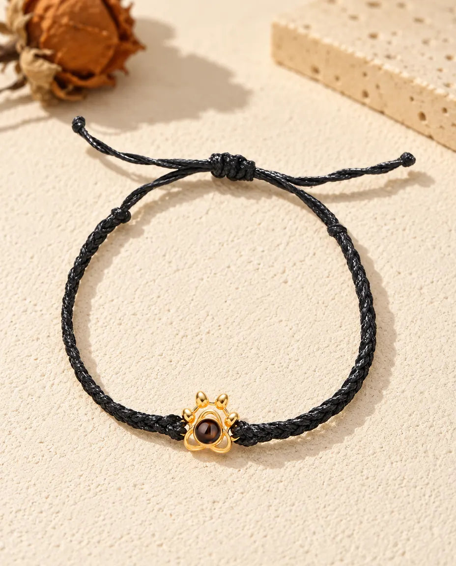 Top view of the gold tone paw charm bracelet on a black braided cord with its sliding knot