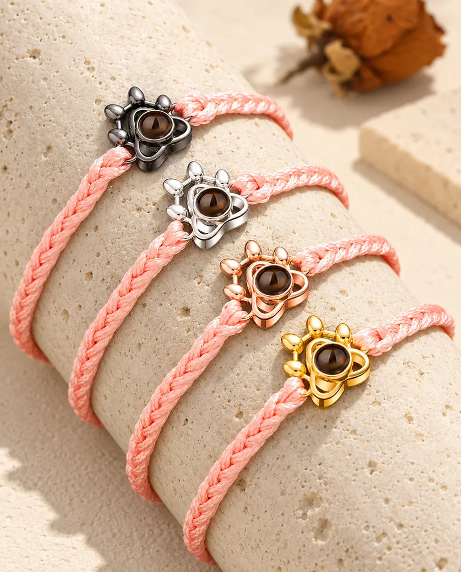 Pink braided cord paw charm bracelets showing every charm color draped over travertine
