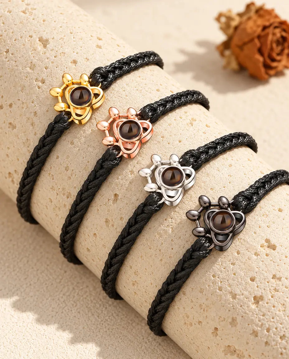 Four black braided cord bracelets with paw charms in each color on a travertine block