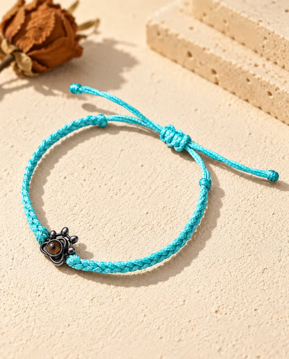 Black paw charm on a blue braided cord holding a brown projection stone