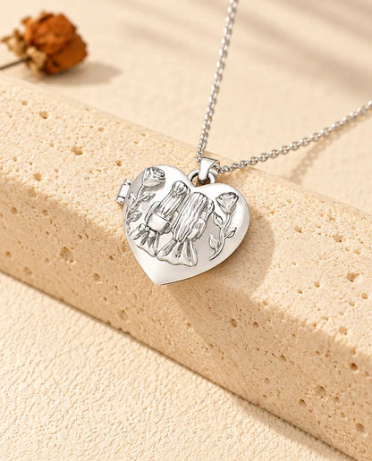 Personalized sisters heart photo locket necklace in silver tone with two girls and roses on the lid, resting on a travertine block