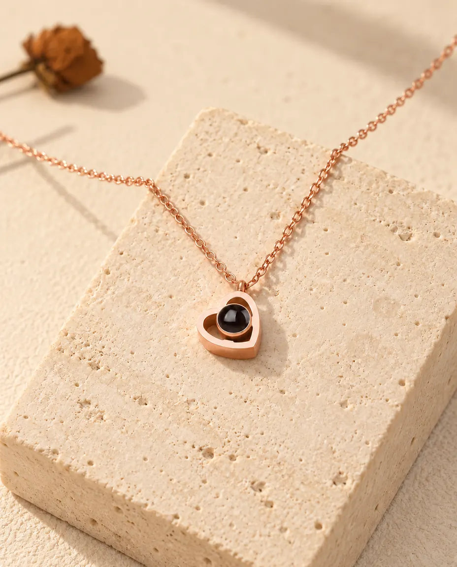 Rose gold tone double heart photo projection necklace draped over a travertine block