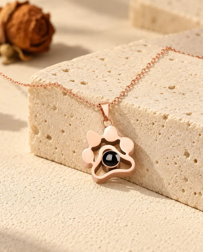 Rose gold tone paw print projection necklace draped over a travertine block