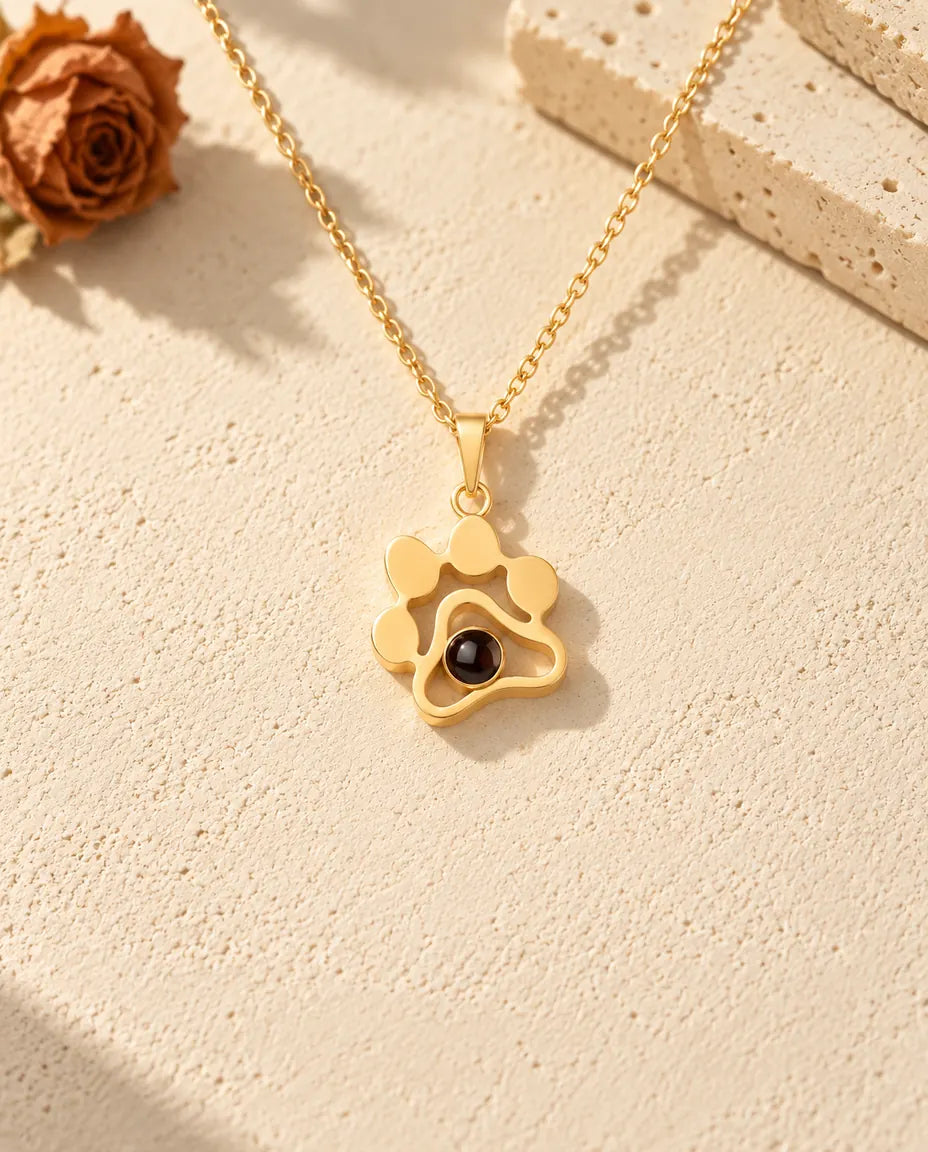 Front view of the gold tone paw print pendant with its dark projection stone