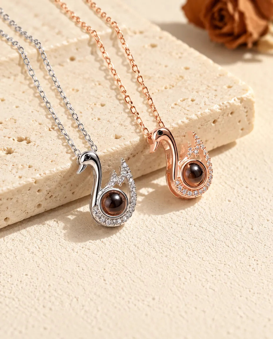 Silver tone and rose gold tone swan photo projection necklaces lying on plaster