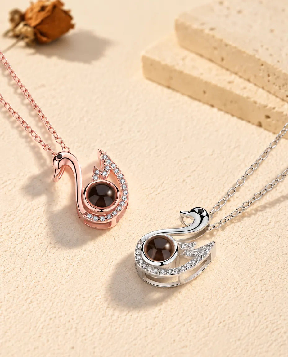 Rose gold tone and silver tone swan necklaces laid diagonally on plaster