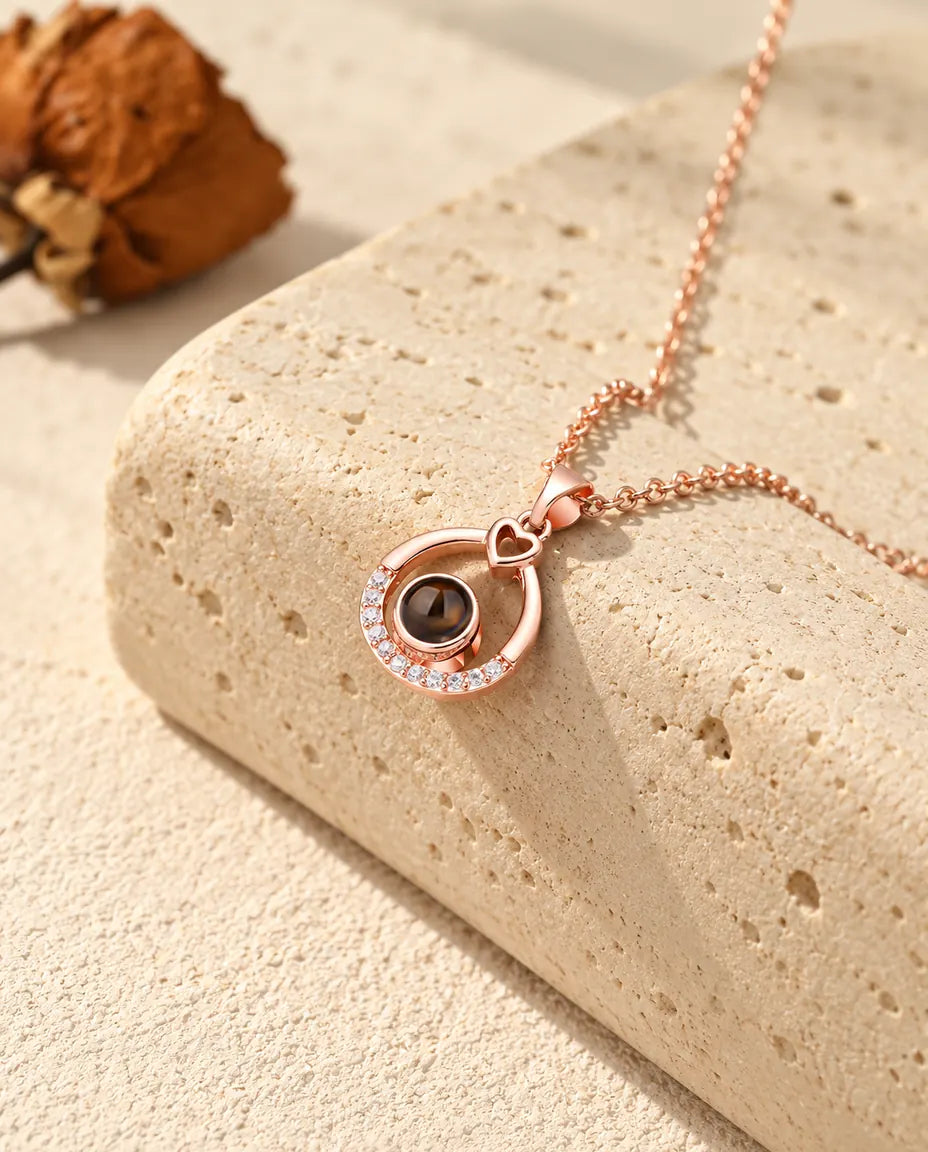 Rose gold tone teardrop projection necklace hanging over travertine