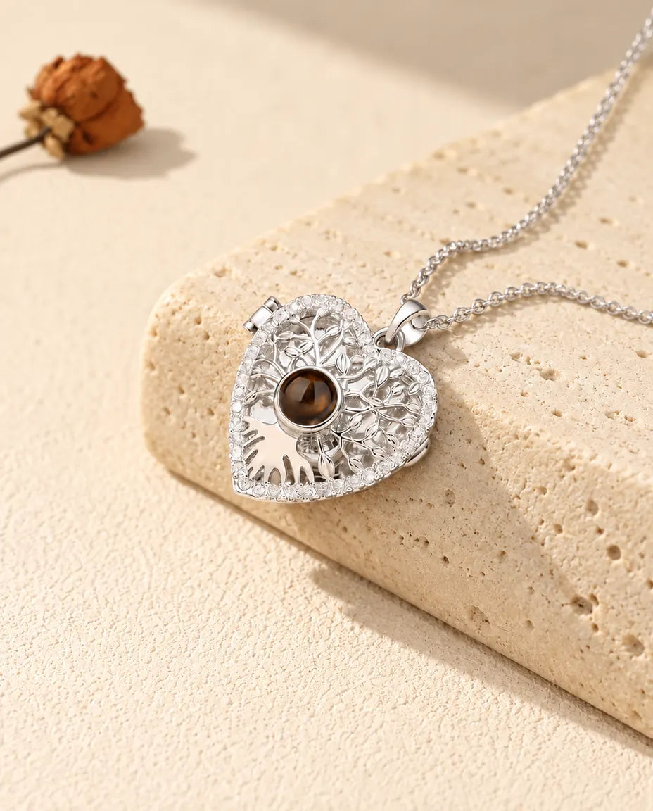 Personalized tree of life heart locket necklace in silver tone with a brown projection stone, resting on a travertine block