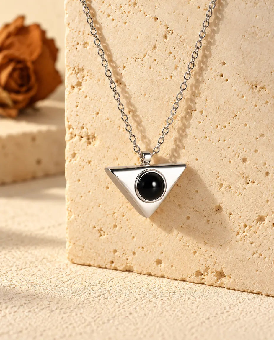 Personalized silver tone triangle photo projection necklace hanging on a travertine block