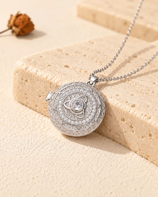 Personalized round trinity knot photo locket necklace in silver tone with cubic zirconia, resting on a travertine block