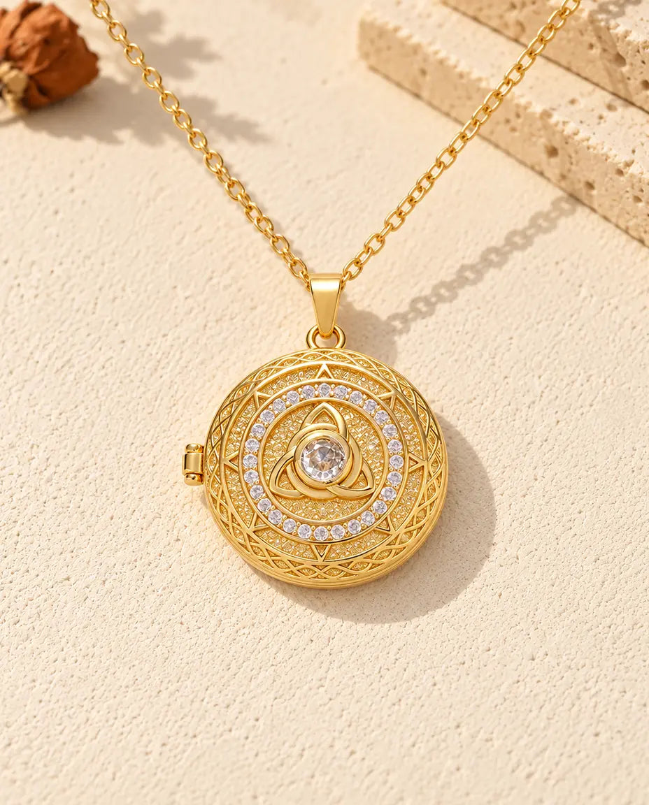 Front view of the gold tone round locket showing the trinity knot, center stone, stone circle and side hinge