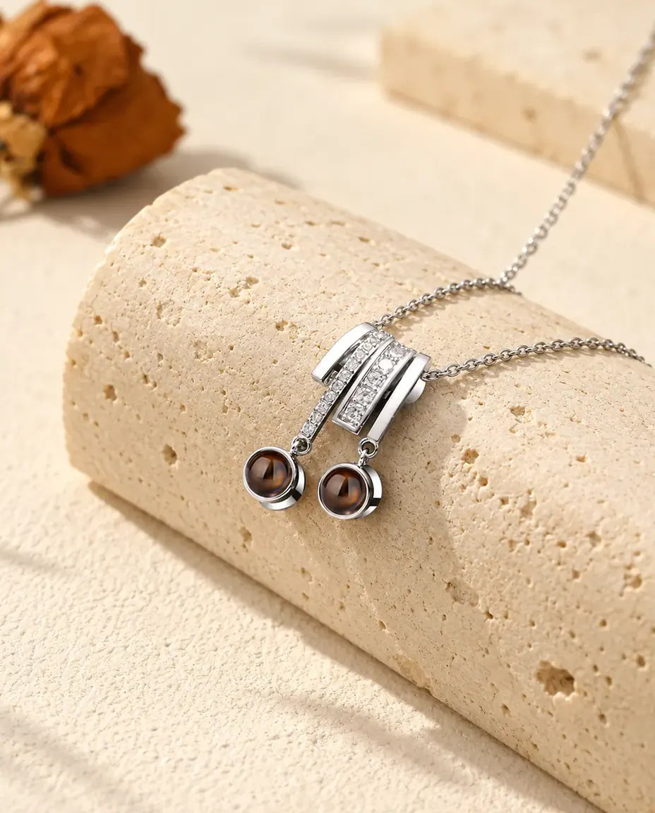Personalized two photo projection necklace in silver tone with a pave slide and two brown projection stones on a travertine block