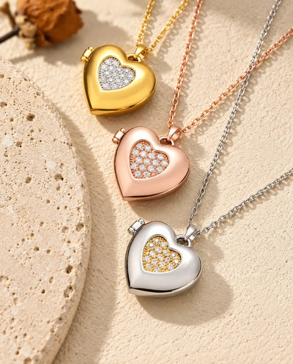 Gold tone, rose gold tone and silver tone two-tone pave heart photo lockets stacked beside a travertine slab