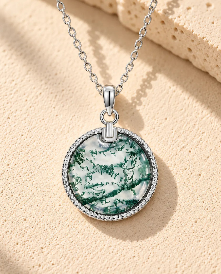 Round Moss Agate Medallion Necklace in 925 Sterling Silver - lying on a cream textured surface beside a travertine block